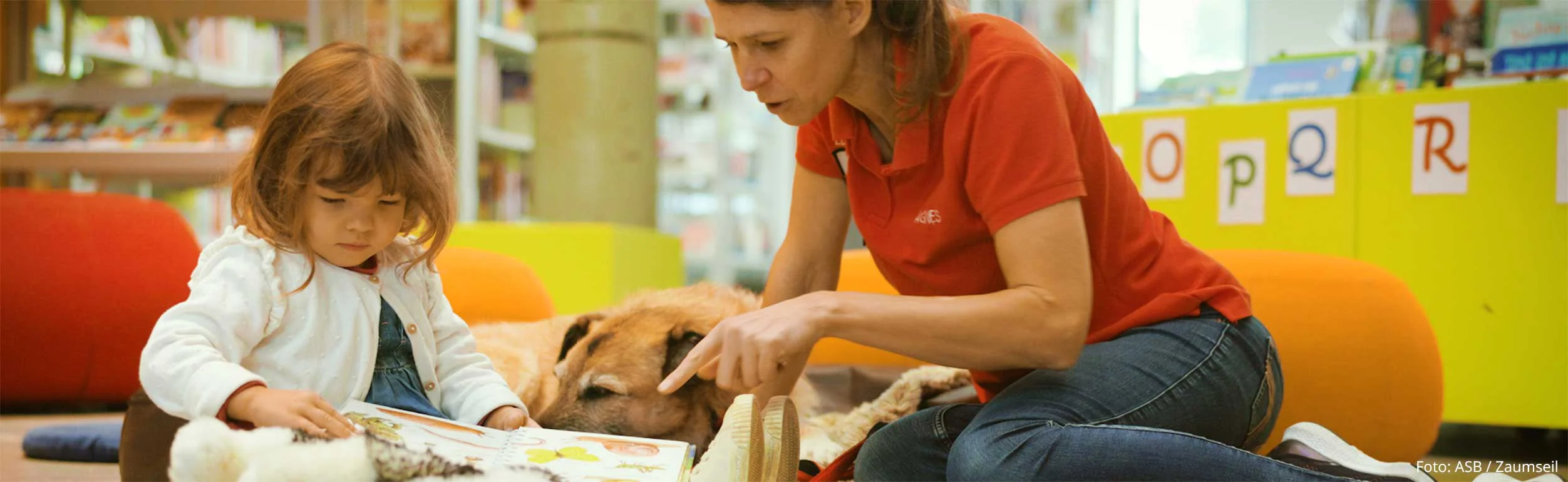 Kleines Mädchen zeigt dem Lesehundeteam ein Buch.