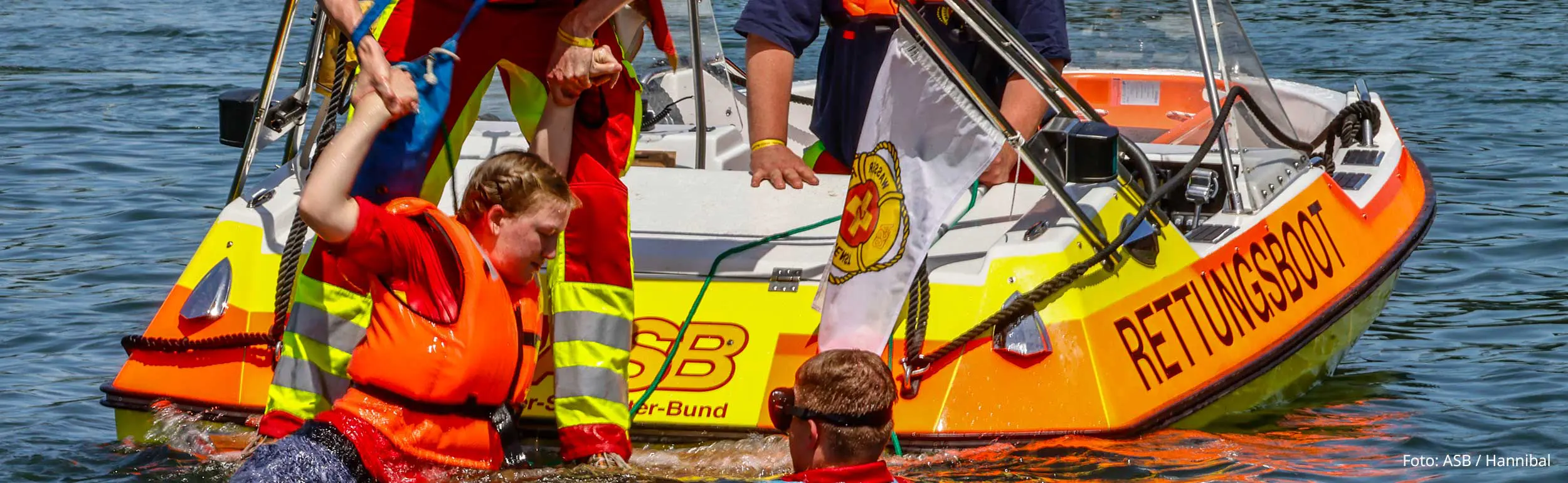 Bevölkerungsschutzübung: Drei Wasserreretter helfen Schwimmerin in Rettungsweste ins Rettungsboot