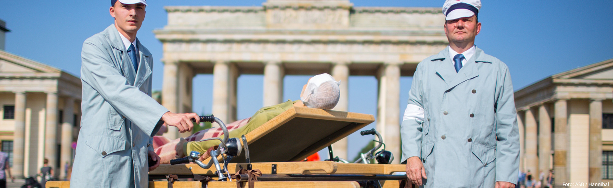 Nachgestelltes historisches Foto mit zwei Samaritern und Holzfahrradtrage vor dem Brandenburger Tor