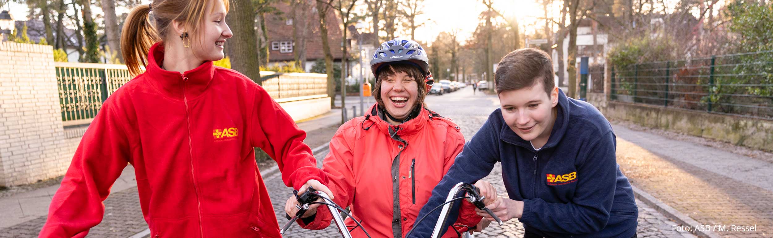 Zwei Freiwilligendienstleistende bringen Bewohnerin der Wohnstätten für Menschen mit Behinderung das Fahrradfahren bei.